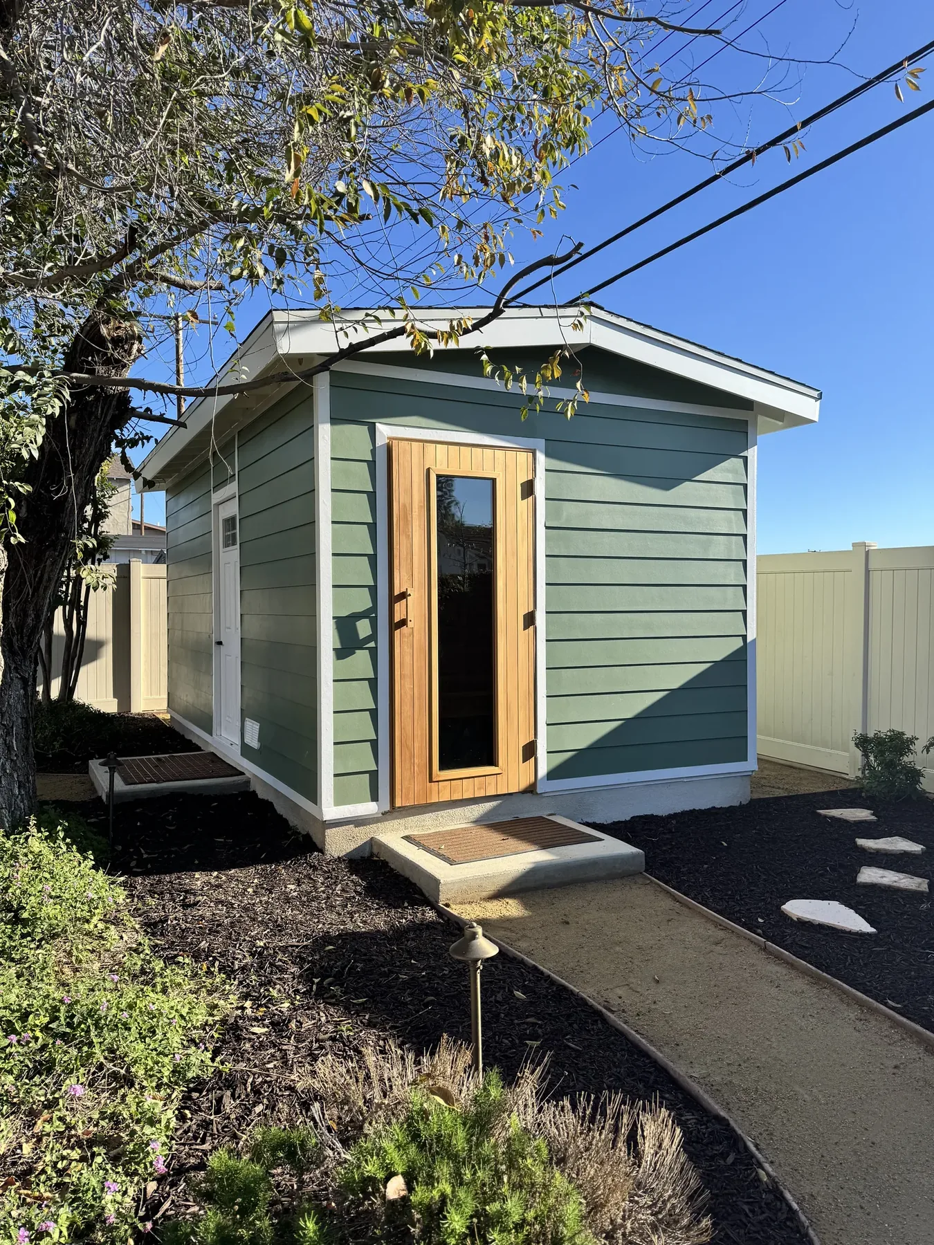 Backyard sauna building with sage green Hardie lap siding, cedar door and single-pitch roof