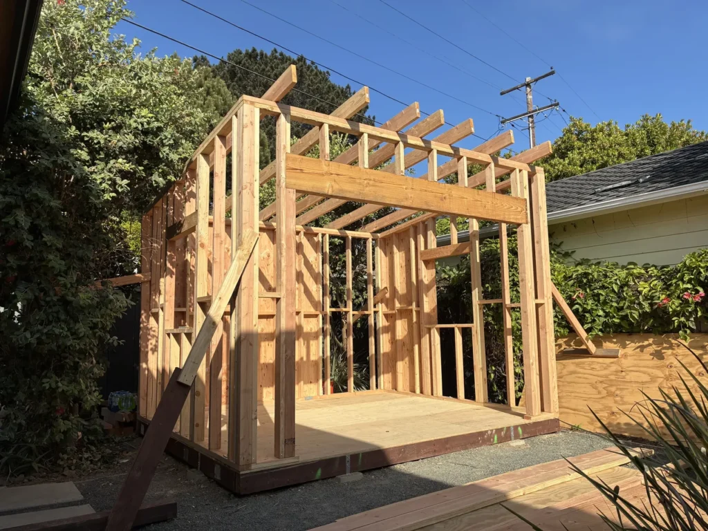 Site-built wall framing with roof rafters set, photographed from the yard