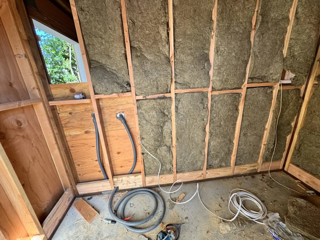 Interior wall framing packed with mineral wool insulation with electrical conduit and boxes roughed in