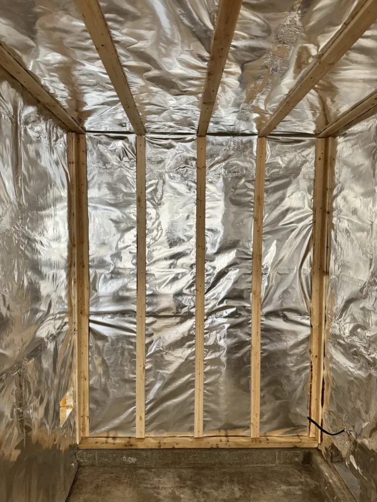 Aluminum foil vapor barrier with taped seams covering the full wall and ceiling of a sauna interior